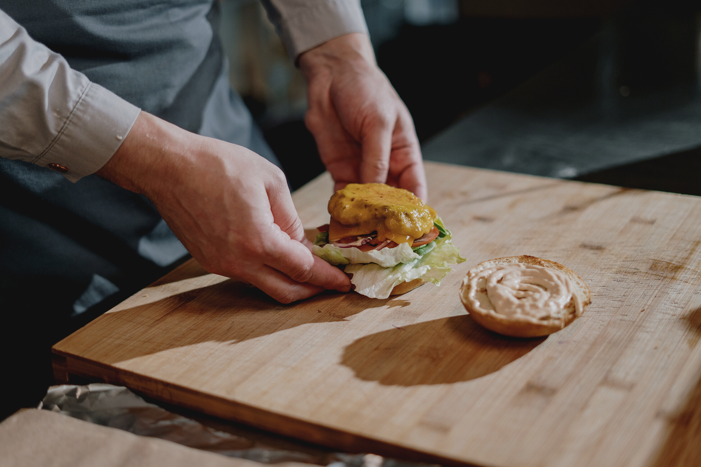 Person Holding Burger on Brown Wooden Chopping Board